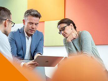 Ein Mann im anzug zeigt einer Frau und einem Mann etwas aug einem Tablet