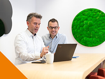 Zwei Männer sitzen in einem Büro und schauen gemeinsam auf einen Laptop
